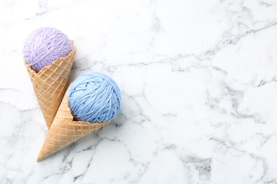 Photo of Ice cream made of colorful yarns and wafer cones on white marble table, flat lay. Space for text