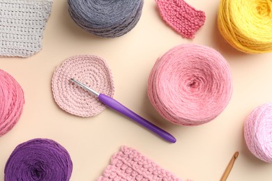 Photo of Different colorful yarns, crochet hook and pattern samples on beige background, flat lay