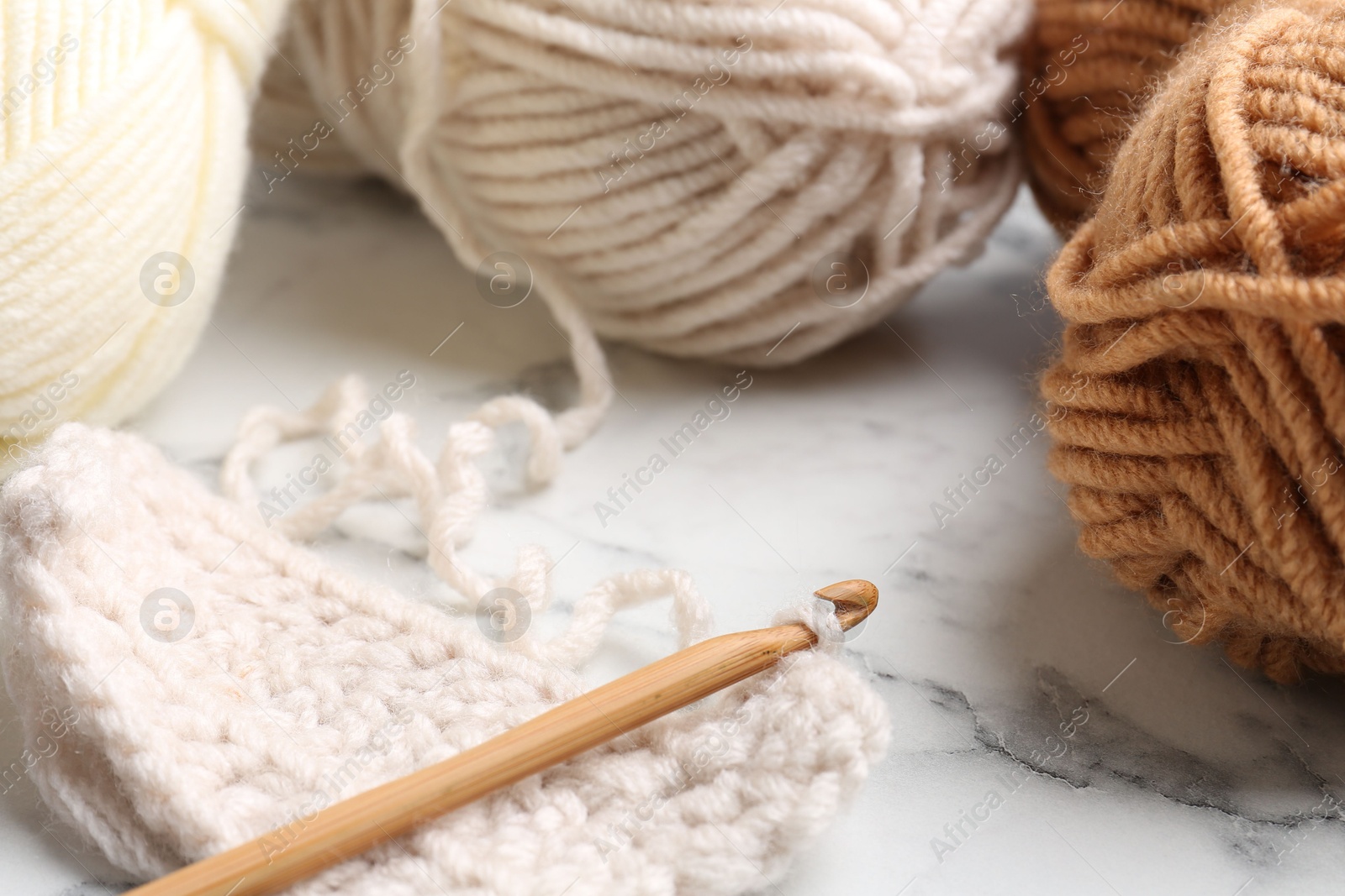 Photo of Crochet hook, pattern samples and colorful yarns on white marble table, closeup