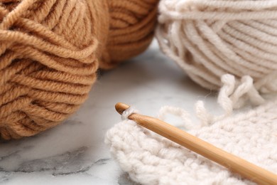 Photo of Crochet hook, pattern samples and colorful yarns on white marble table, closeup