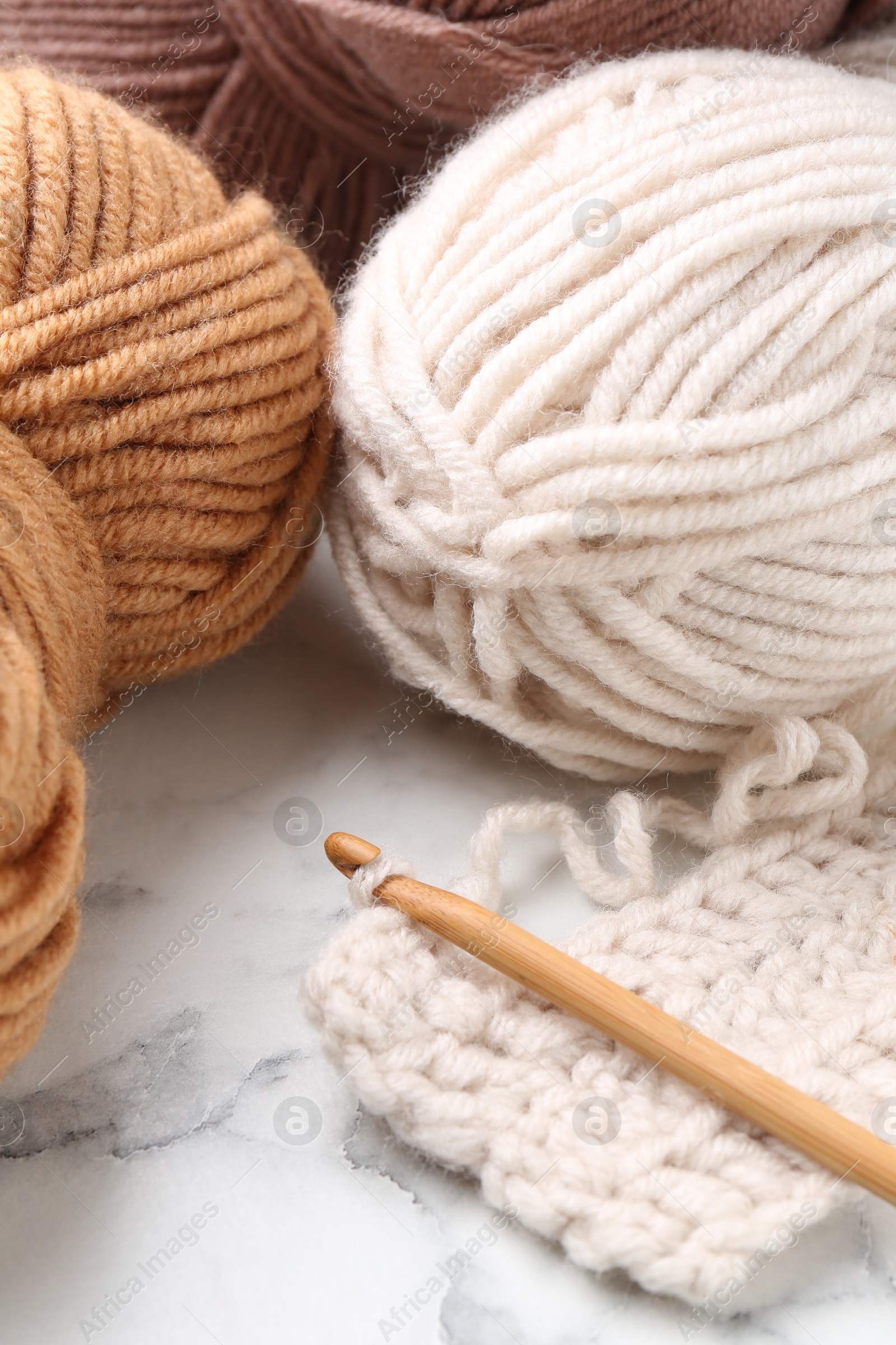 Photo of Crochet hook, pattern samples and colorful yarns on white marble table, closeup