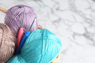 Photo of Crochet hooks and colorful yarns on white marble table, closeup. Space for text