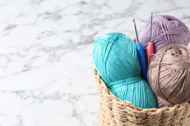 Photo of Crochet hooks and colorful yarns in wicker basket on white marble table, closeup. Space for text