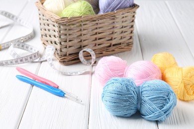 Photo of Crochet hooks, measuring tape and colorful yarns on white wooden table, closeup