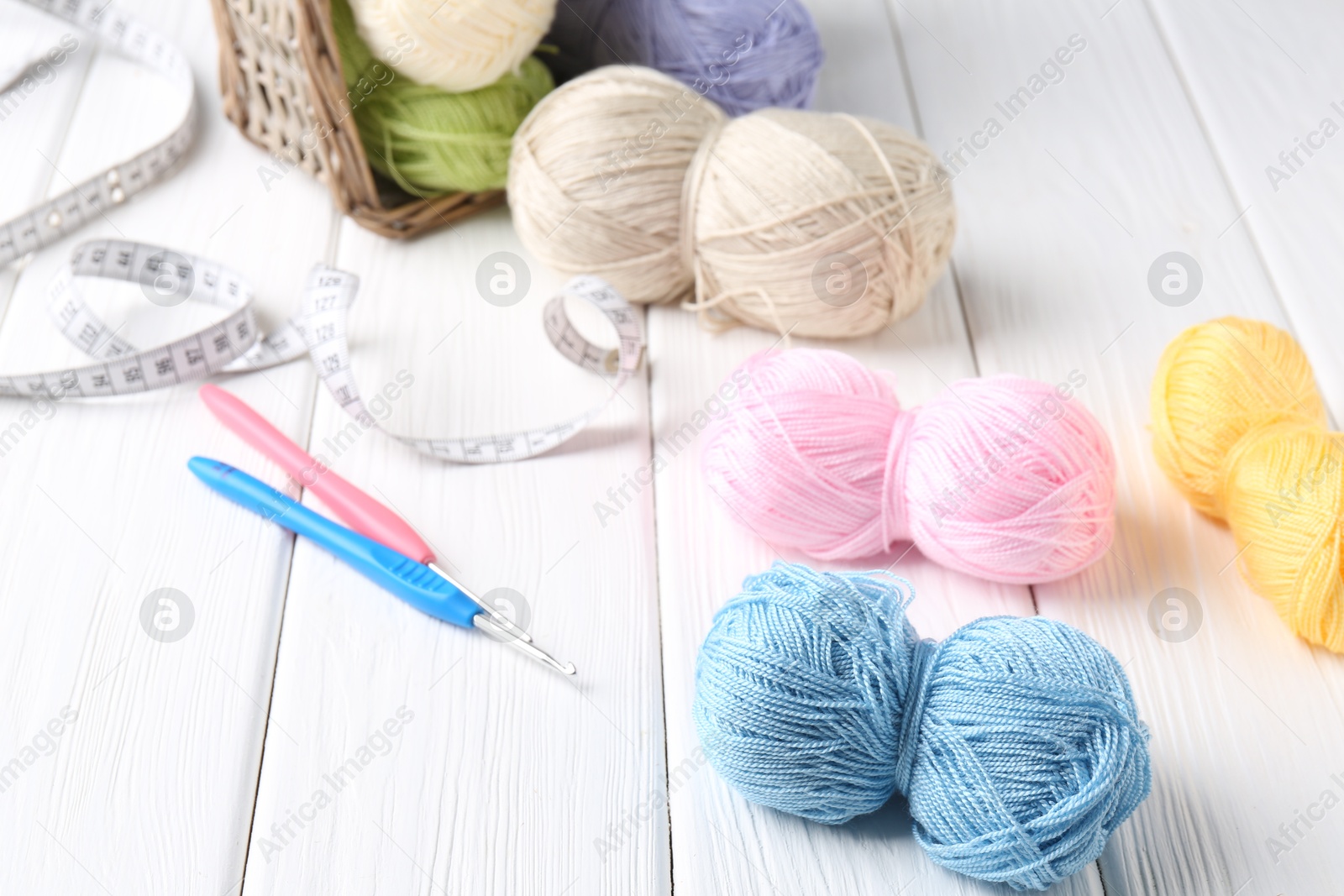 Photo of Crochet hooks, measuring tape and colorful yarns on white wooden table, closeup