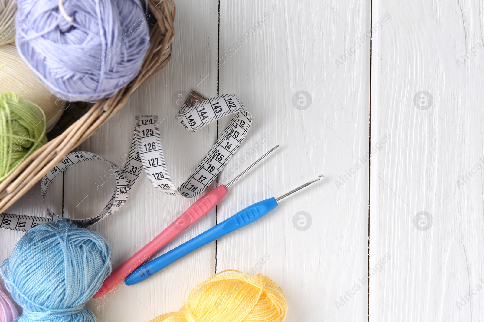 Photo of Crochet hooks, measuring tape and colorful yarns on white wooden table, flat lay. Space for text