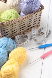 Photo of Crochet hooks, measuring tape and colorful yarns on white wooden table, closeup