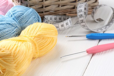 Photo of Crochet hooks, measuring tape and colorful yarns on white wooden table, closeup