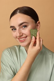 Photo of Beautiful young woman doing facial massage with gua sha tool on beige background