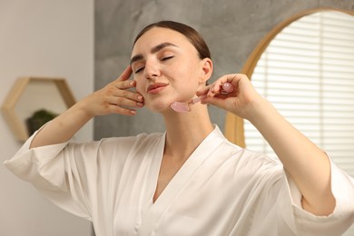 Photo of Beautiful young woman doing facial massage with roller at home
