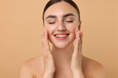 Beautiful young woman doing facial massage on beige background