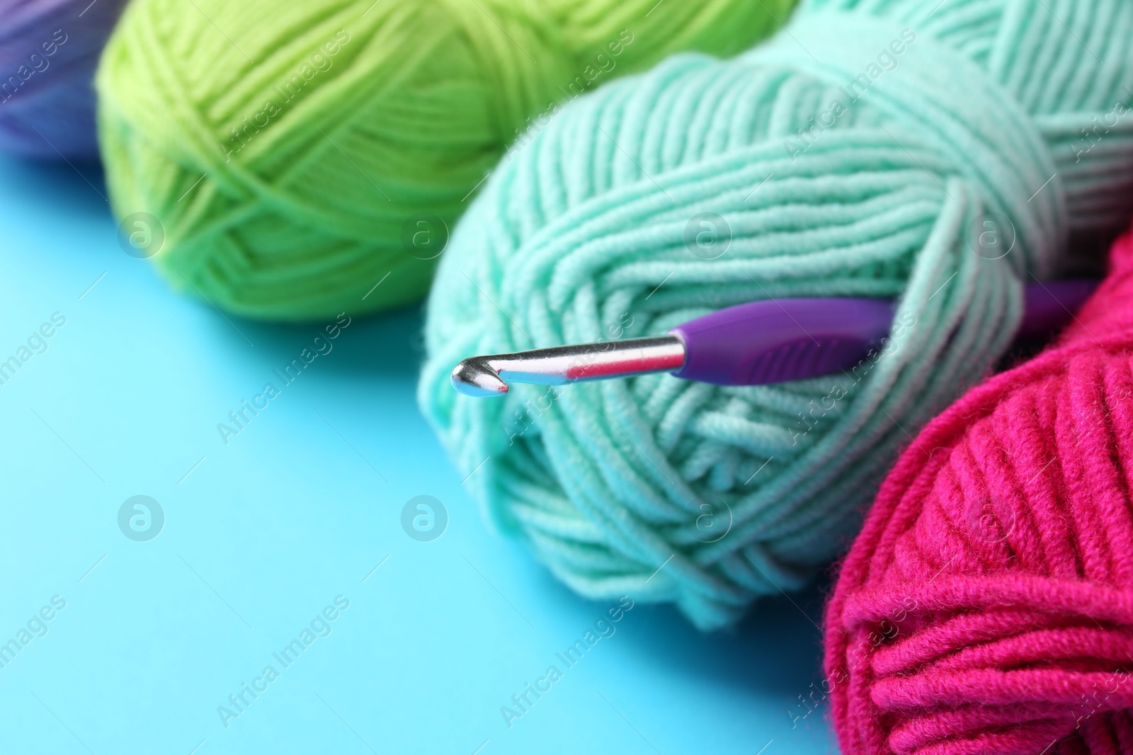 Photo of Colorful yarns and crochet hook on light blue background, closeup