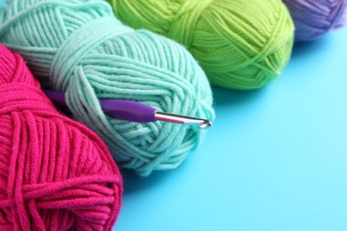 Photo of Colorful yarns and crochet hook on light blue background, closeup