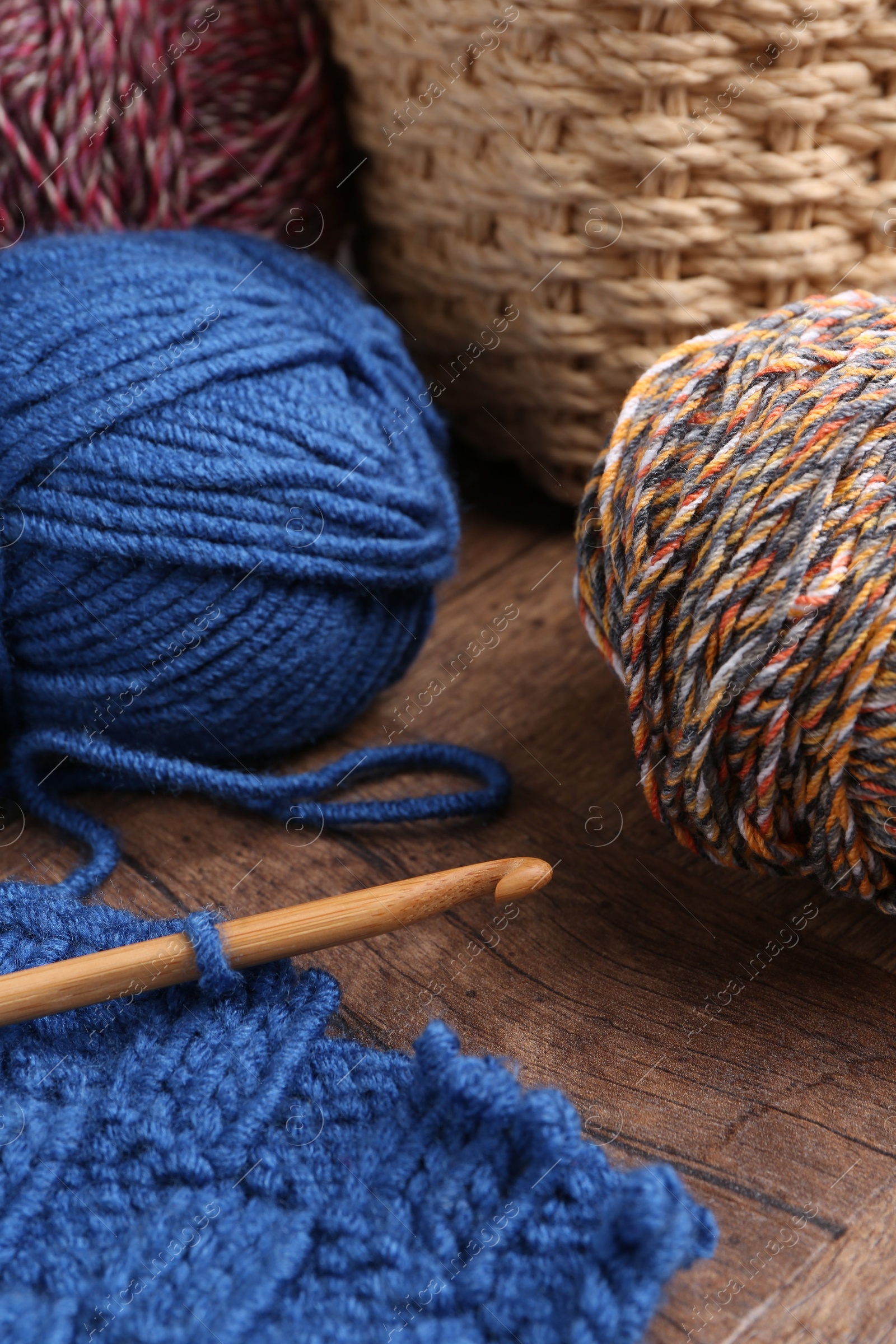 Photo of Colorful yarns, pattern sample and crochet hook on wooden table, closeup