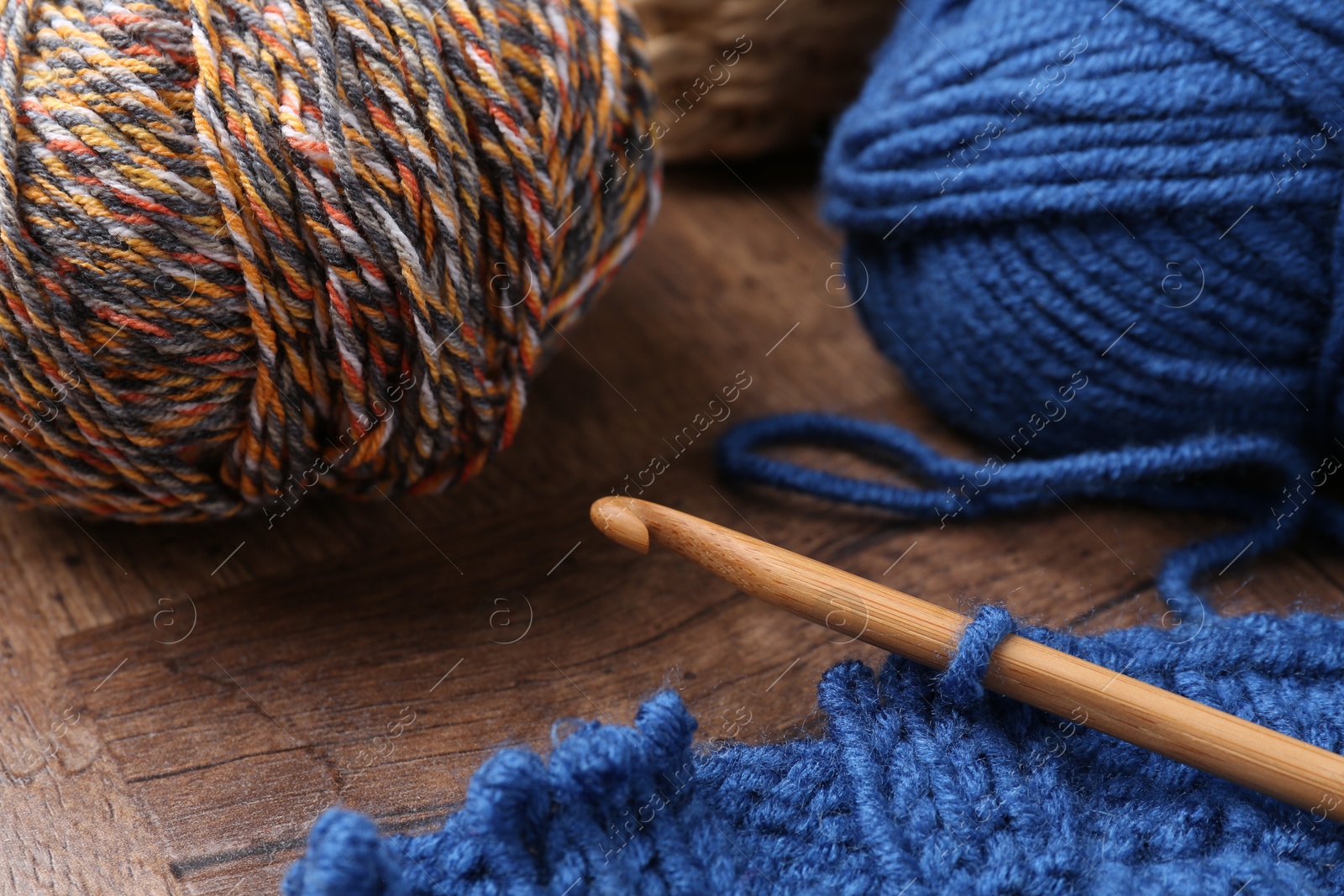 Photo of Colorful yarns, pattern sample and crochet hook on wooden table, closeup