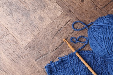 Photo of Blue yarns, pattern sample and crochet hook on wooden table, top view. Space for text