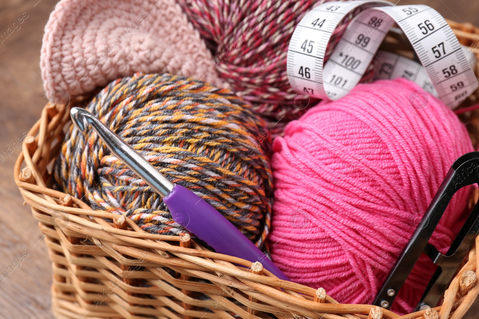 Photo of Colorful yarns, measuring tape and crochet hook in wicker basket on table, closeup