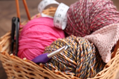 Photo of Colorful yarns, measuring tape and crochet hook in wicker basket, closeup