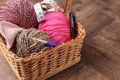 Photo of Colorful yarns, measuring tape and crochet hook in wicker basket on wooden table, closeup