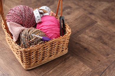 Photo of Colorful yarns, measuring tape and crochet hook in wicker basket on wooden table. Space for text