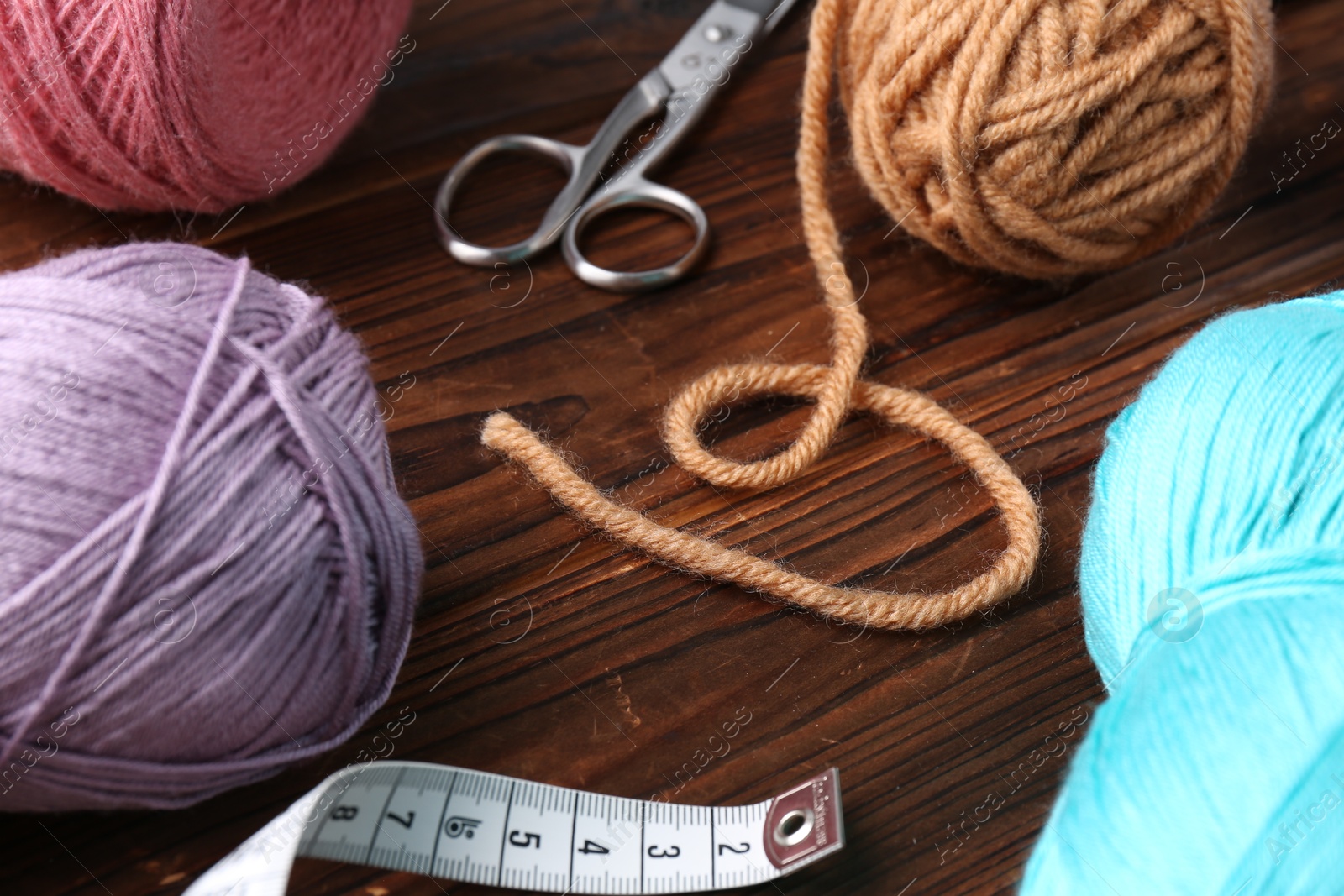 Photo of Colorful yarns, measuring tape and scissors on wooden table, closeup