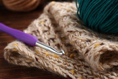 Photo of Crochet hook, sweater and yarn on wooden table, closeup