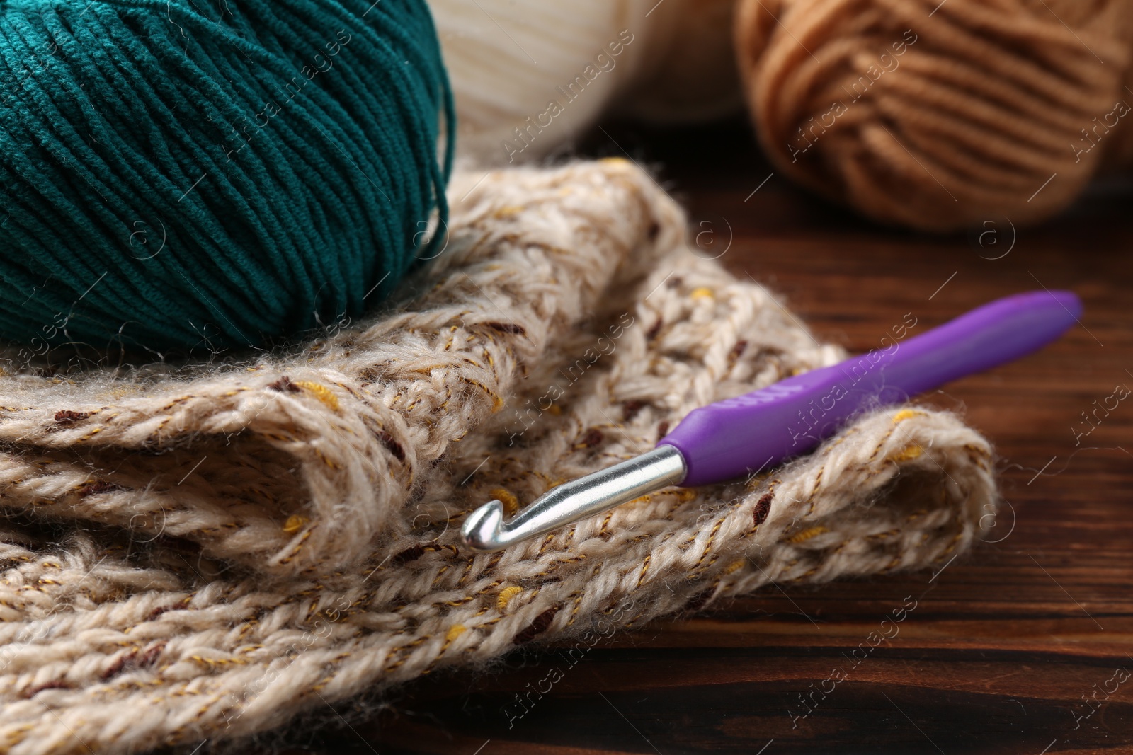 Photo of Crochet hook, sweater and yarn on wooden table, closeup