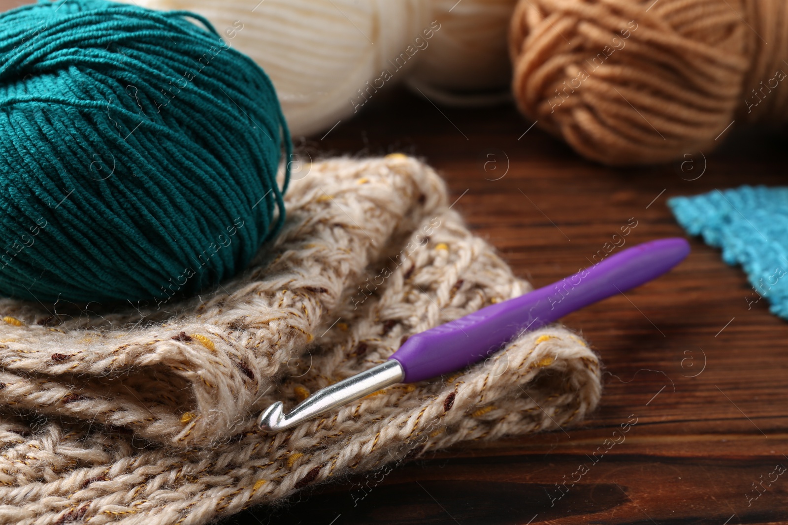 Photo of Crochet hook, sweater and yarn on wooden table, closeup