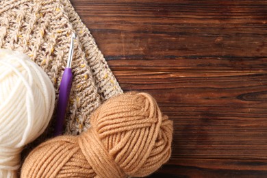 Photo of Crochet hook, sweater and skeins of yarn on wooden table, top view. Space for text