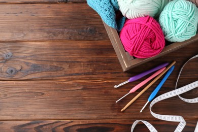 Photo of Crochet hooks, different yarns and measuring tape on wooden table, flat lay. Space for text