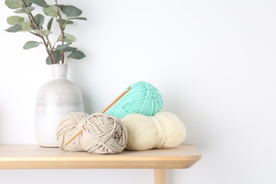 Photo of Skeins of yarn, eucalyptus in vase and crochet hook on wooden shelf. Space for text