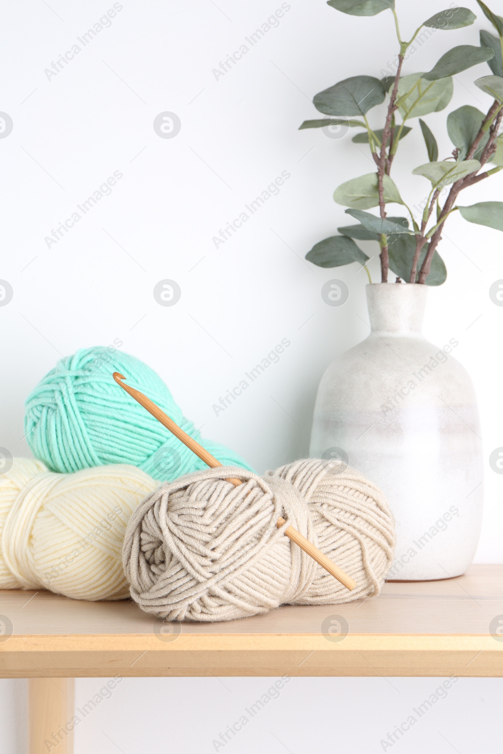 Photo of Skeins of yarn, eucalyptus in vase and crochet hook on wooden shelf