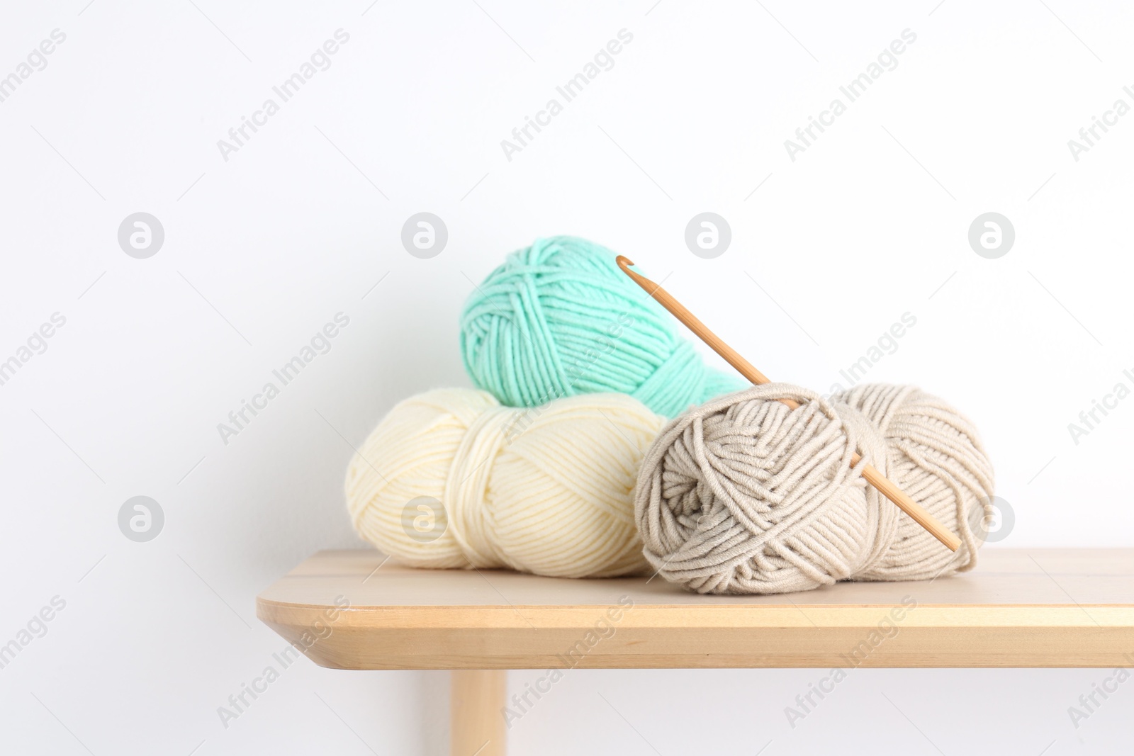 Photo of Skeins of yarn and crochet hook on wooden shelf. Space for text