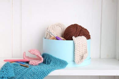 Photo of Different yarns, pattern samples and crochet hooks on white shelf