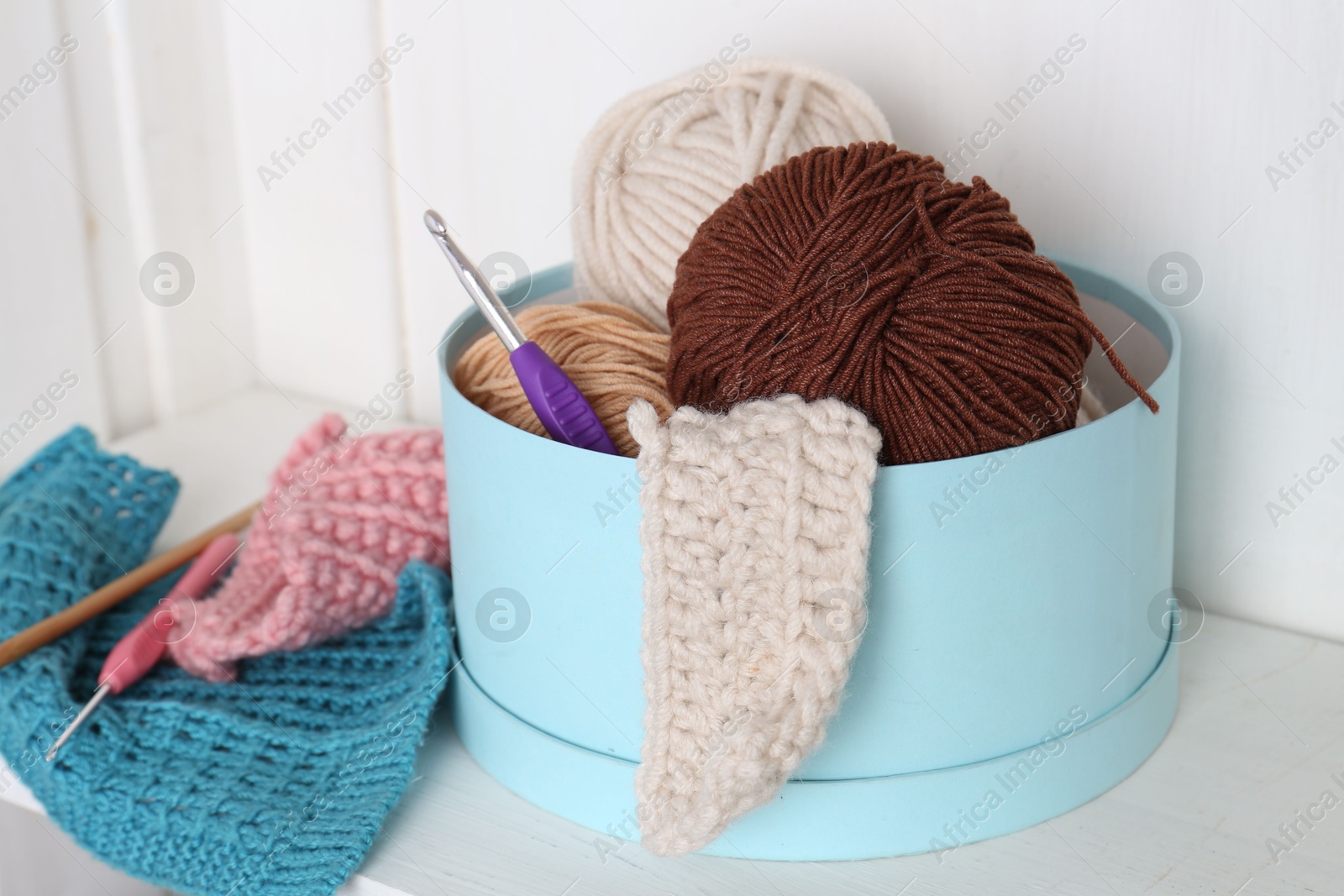 Photo of Different yarns, pattern samples and crochet hooks on white shelf