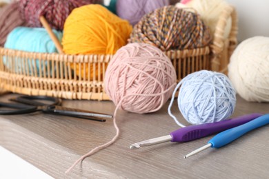 Photo of Different yarns, crochet hooks and scissors on wooden shelf, closeup