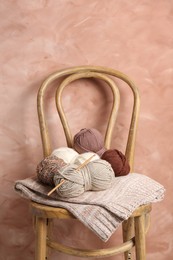 Photo of Different yarns, crochet hook and project on chair near beige wall