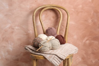 Photo of Different yarns, crochet hook and project on chair near beige wall