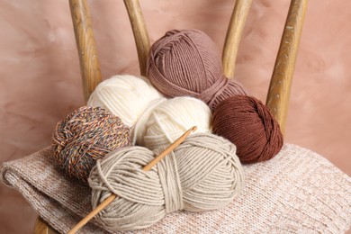 Photo of Different yarns, crochet hook and project on chair near beige wall, closeup