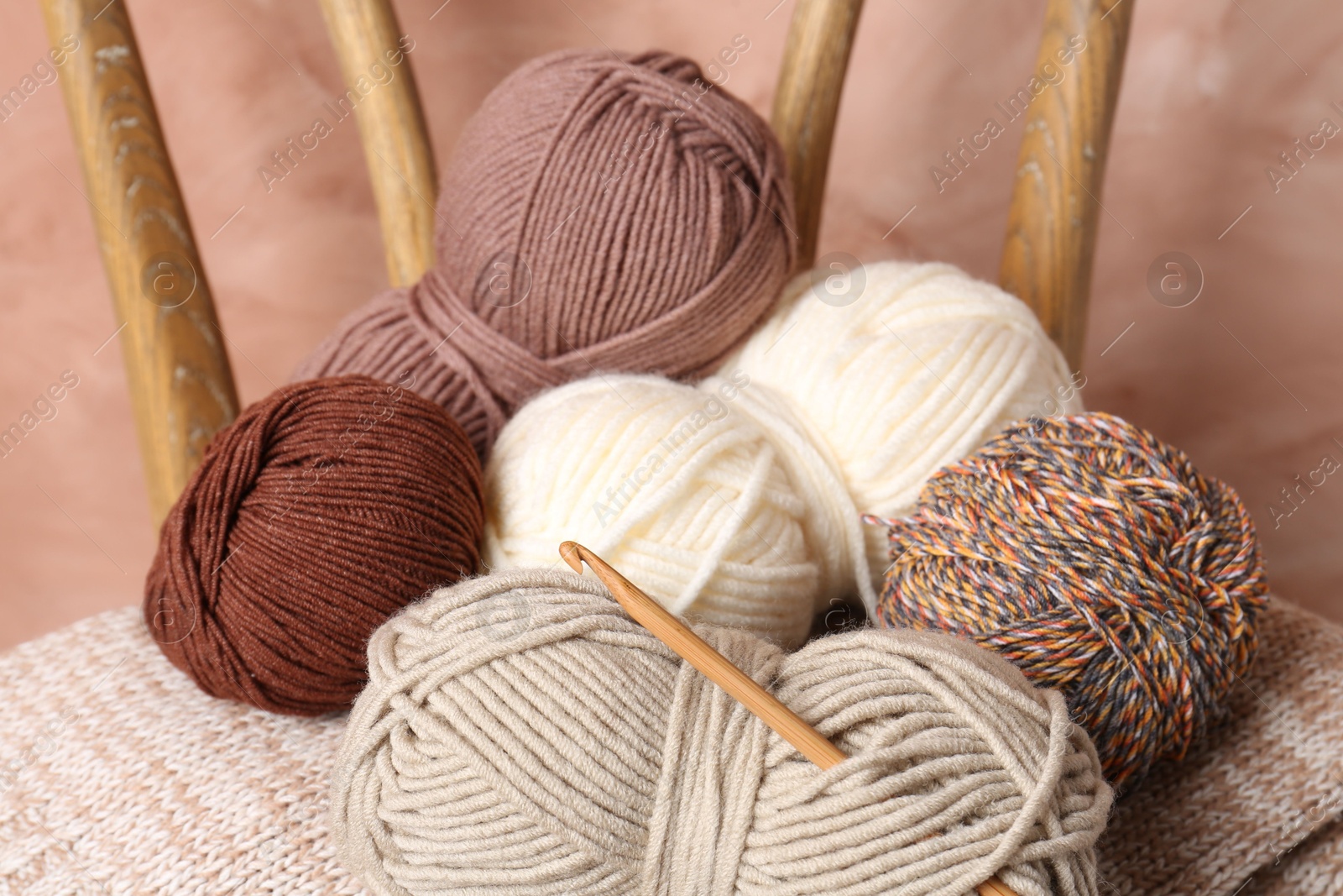 Photo of Different yarns, crochet hook and project on chair near beige wall, closeup