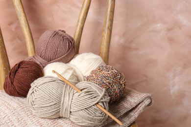 Photo of Different yarns, crochet hook and project on chair near beige wall, closeup. Space for text