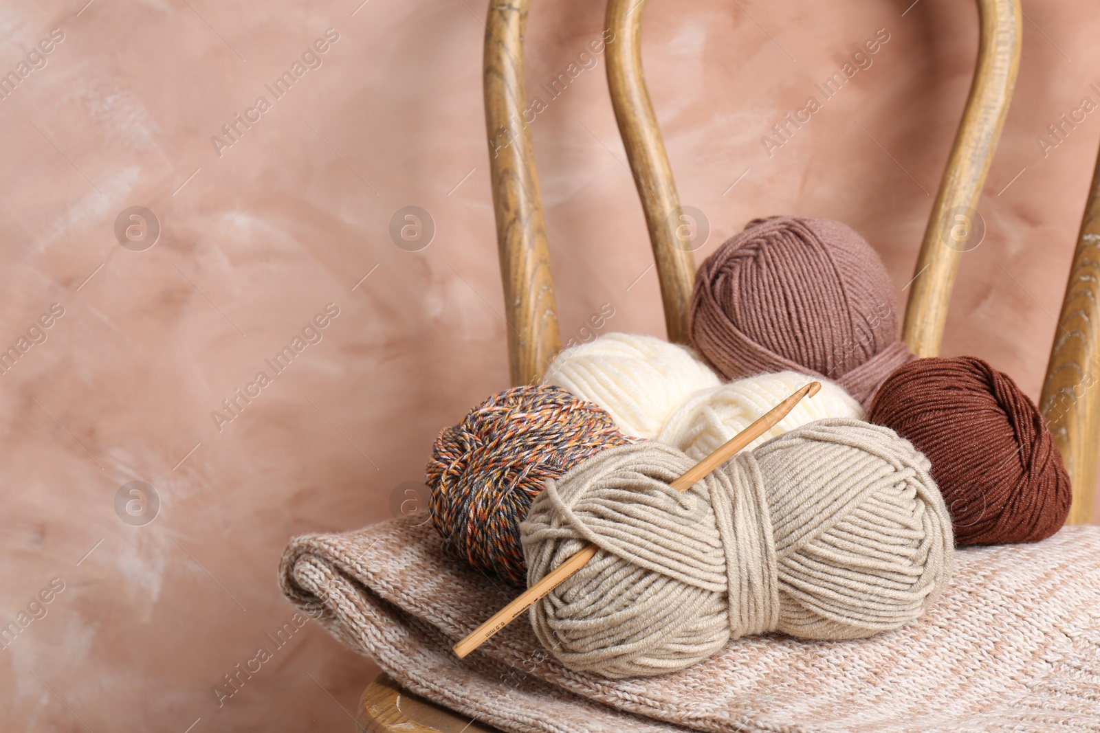 Photo of Different yarns, crochet hook and project on chair near beige wall, closeup. Space for text