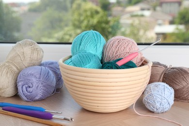 Photo of Different yarns and crochet hooks on wooden sill near window