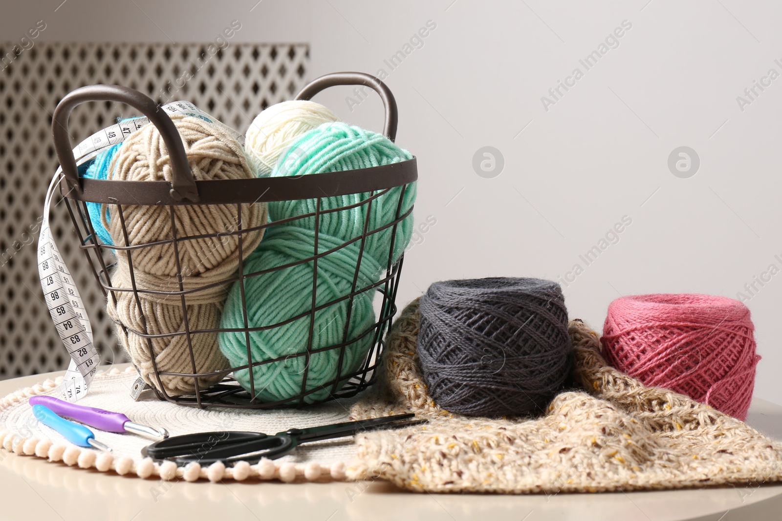 Photo of Different yarns, crochet hooks, pattern sample and scissors on beige table