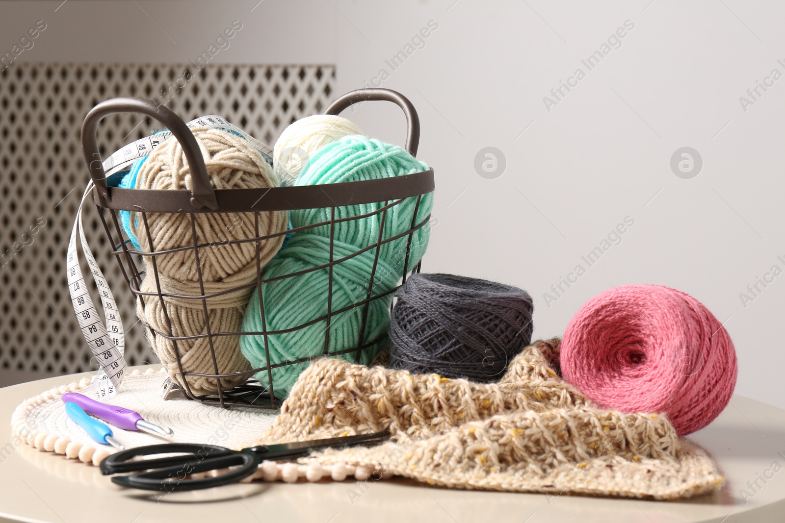 Photo of Different yarns, crochet hooks, pattern sample and scissors on beige table