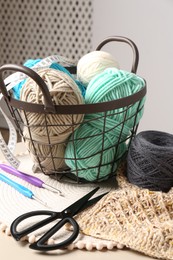 Photo of Different yarns, crochet hooks, pattern sample and scissors on table