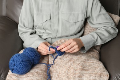 Photo of Woman crocheting with hook on sofa, closeup