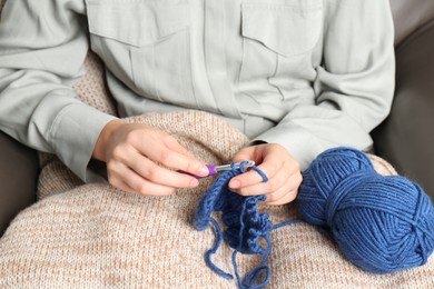 Photo of Woman crocheting with hook and blue yarn, closeup