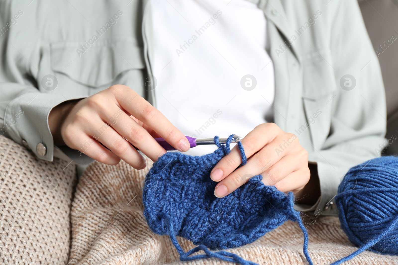 Photo of Woman crocheting with hook and blue yarn, closeup