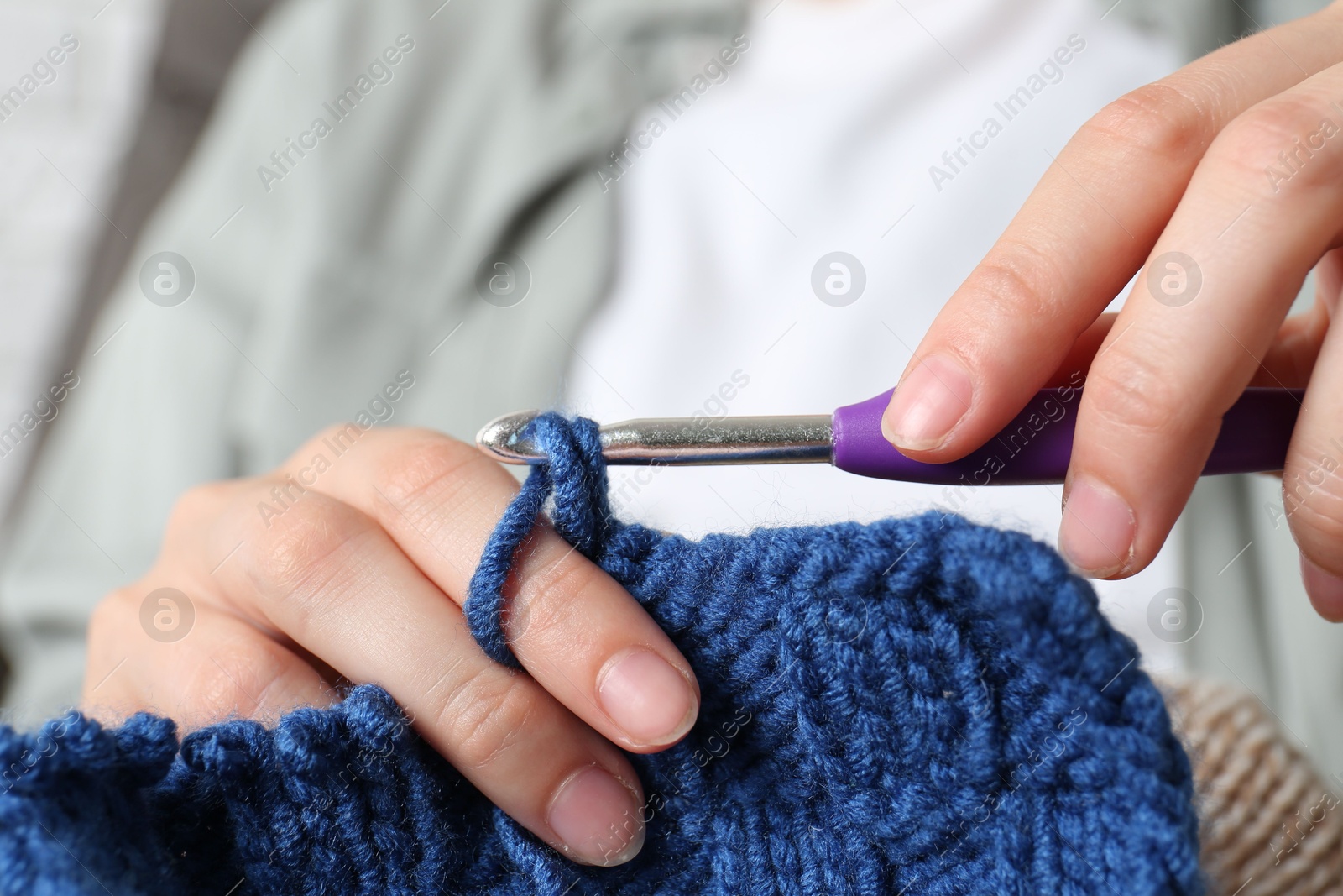 Photo of Woman crocheting with hook and blue yarn, closeup